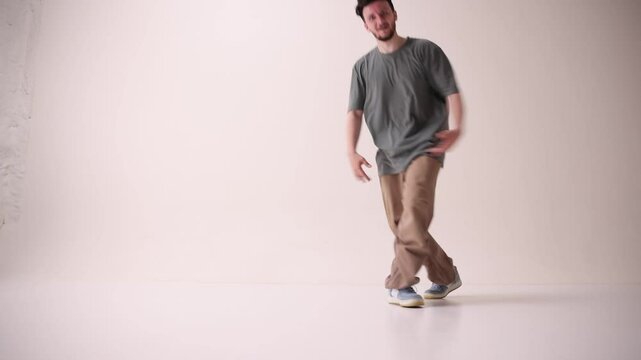 Young athletic man dressed streetstyle clothes dancing modern breakdance against white studio background. Concept of art and sport, music, creativity, fashion and style.