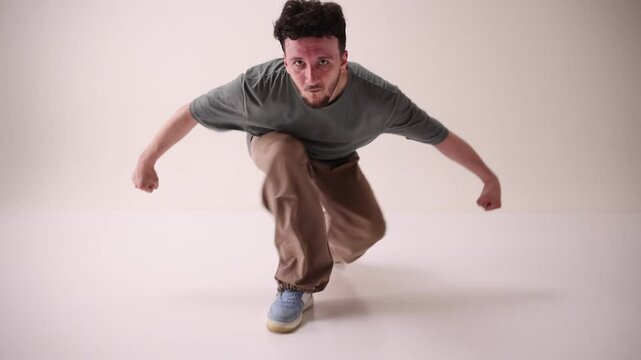 Talented dancer, young athletic man dressed streetstyle outfit and moves in music rhythm against white studio background. Concept of art and sport, music, creativity, fashion and style.