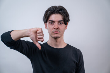 Young man showing a thumb down sign with a serious expression on isolated white background.