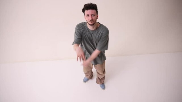 Aer view of talented dancer, young athletic man dressed streetstyle outfit dancing beak-dance against white studio background. Concept of art and sport, music, creativity, fashion and style.