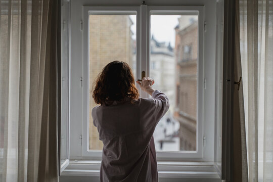 Young woman opens or closes window handle in apartment, back view