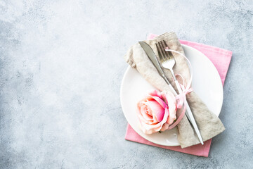 Table setting, festive table serving with white plate, modern cutlery and pink flowers. Top view at white with copy space.
