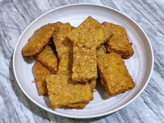 Crispy flour fried tempeh, served on a white plate.