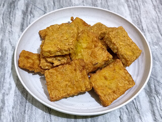 Crispy flour fried tempeh, served on a white plate.