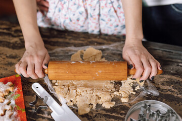 A close-up of hands holding a rolling pin, rolling out dough for cookies.