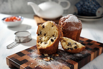 Cooked chocolate chip muffins on a beautiful wooden board with a teapot and cups in the background.