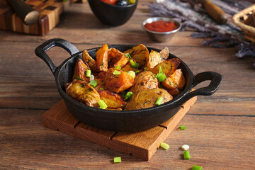 Cooked potatoes with onions and dill in a black cast iron frying pan on a wooden table.