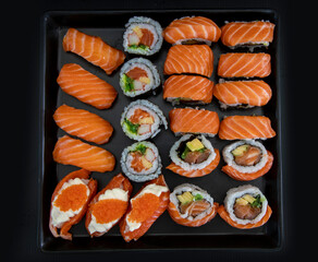 Black plate with Japanese sushi, tuna maki rolls, salmon nigiri, salmon nigiri with cream cheese and crab roe