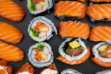 Black plate with Japanese sushi, tuna maki rolls, salmon nigiri, salmon nigiri with cream cheese and crab roe