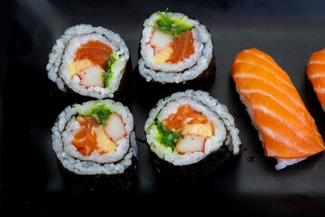 Japanese salmon maki rolls and salmon nigiri on black plate
