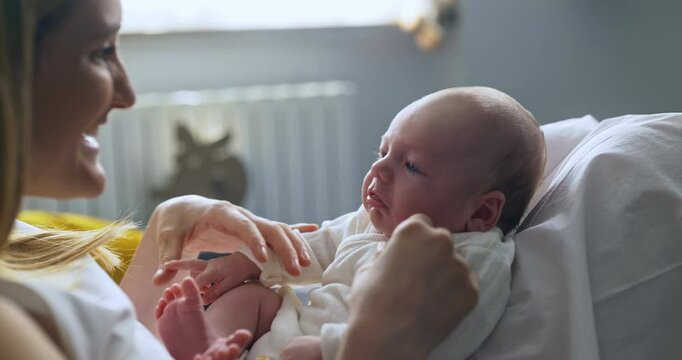 A caring mother communicating and mocking or joking with her new born child. Mom playing with son at home on the sofa. Young female mother holding her loving child on her knees while talking to him.