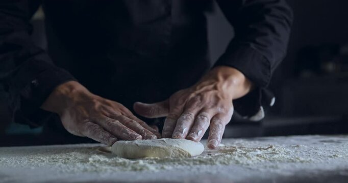Pizza maker making fresh pizza from a piece of Dough. Experienced Chef Kneading fresh Pasta. Pizzaiolo making Food in bakery. Pizzeria restaurant making handmade pizza on steel table with Flour.