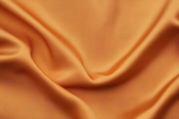 A close-up view of smooth, flowing orange fabric, showcasing its texture and subtle sheen.