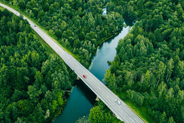 Aerial view of asphalt road with cars over blue river and green summer woods in Finland, drone photography