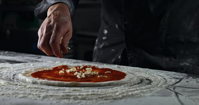 Pizza maker makes fresh Italian pizza from a piece of dough. Experienced Chef drop mozzarella cheese on tomato sauce pizza. Pizzaiolo making food in bakery. Pizzeria restaurant making handmade pizza.