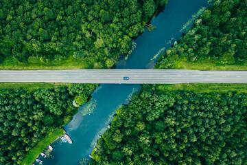 Aerial view of asphalt road with cars over blue river and green summer woods in Finland, drone photography
