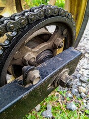 This close-up photo captures a motorcycle chain and sprocket covered in grease and dirt.  The bolts and metal components show signs of wear, while the background consists of gravel and grass.