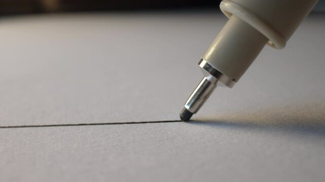 Macro close-up of fineliner pen drawing straight line on white paper, ink flow