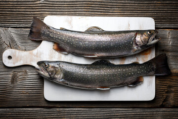 Two arctic char fish on white wooden cutting board on rustic table. Freshwater river trout close up. Food photography