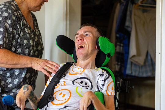 Middle aged woman fixing wheelchair strap on son with disability