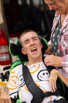 Middle aged woman checking straps on son with disability on the wheelchair.
