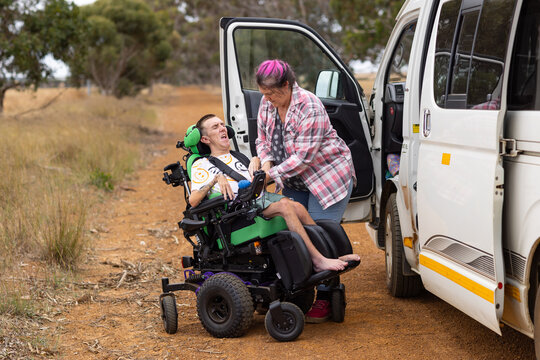 Middle aged woman checking straps on son with disability on the wheelchair