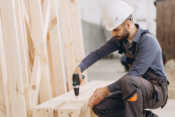 Carpenter using cordless drill assembling wooden structure in workshop