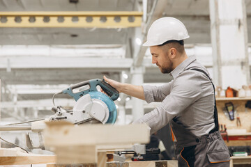 Carpenter cutting wooden plank with circular saw in workshop
