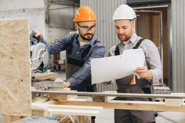 Construction workers building modular housing using circular saw and blueprint