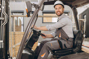 Construction worker driving forklift in modular building factory