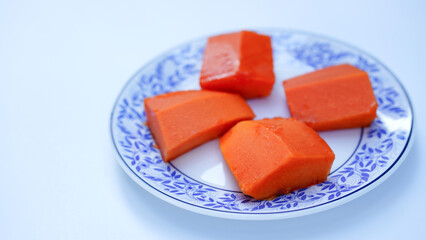 a top view of plate of diced papaya.  Chopped papaya fruit in a plate on a white background.