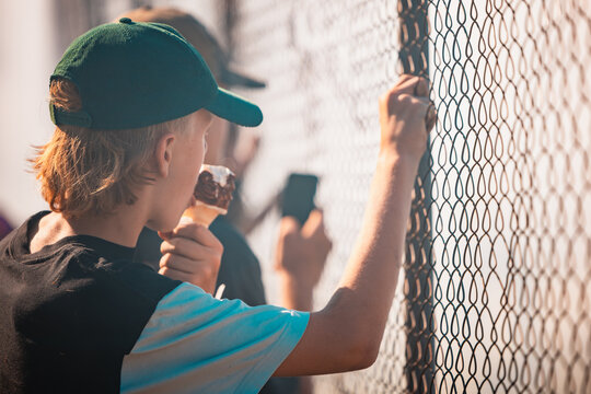 Teenagers watching vehicle burnout competition through chain mesh fence with smoke haze from burning