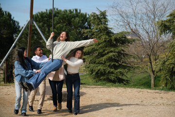 Group of young adults playing together with a zip line in a park during a sunny day