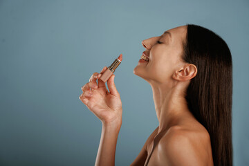 Obraz premium Applying lipstick. Young woman is in the studio against background