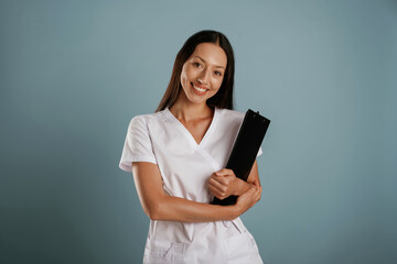 Fototapeta premium In professional lab coat, nurse is standing. Young woman is in the studio against background