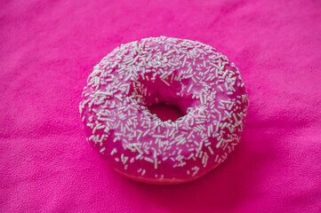 Bright pink frosted donut covered in white sprinkles sitting on a vibrant pink backdrop