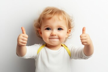 Little child showing thumbs up with a joyful expression, against a plain background during daytime playful moment