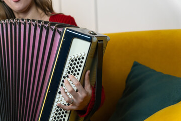 Close-up of female musician's hand playing a traditional accordion, with a blurred yellow sofa in...