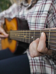 Close-up of a musician's hands playing an acoustic guitar, practicing chords on the fretboard,...