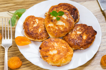 Cottage cheese pancakes with dried apricots and honey on a wooden table