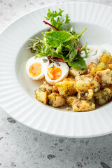 A beautifully presented dish featuring golden roasted potatoes, soft-boiled eggs with runny yolks, and a fresh green salad drizzled with a creamy dressing on a textured plate.