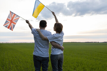 unrecognizable man and woman standing hugging and holding Ukrainian and British flags against sky. Unity and support for Ukraine. International friendship and cooperation in ending war with Russia