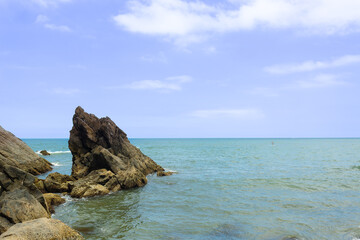 View of the sea with rocks in the foreground, in the background an athlete practicing stand up paddle.