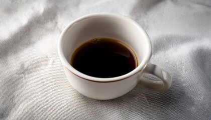 small white ceramic cup with small speckles on it sitting on a white cloth the cup appears to be empty and is filled with a dark liquid possibly coffee or tea