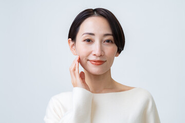 白背景で肌に触れ微笑むショートヘアーの女性