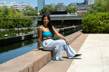 Fototapeta premium Young latin woman relaxing by city park pond in summer