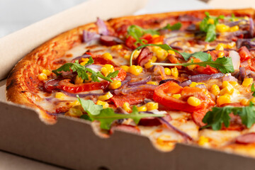 Large Pizza with sausages peppers and sweetcorn in open carton box on kitchen table extreme closeup view