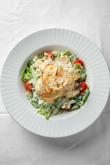 Fresh Caesar salad with grilled chicken, cherry tomatoes, and crispy bread slices, presented in a stylish white bowl. Perfect for healthy dining and gourmet cuisine.
