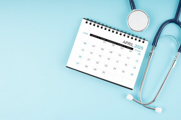 April 2025 desk calendar and stethoscope on blue, Position with copy space.