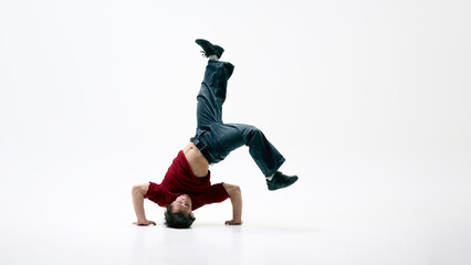 Breakdancer executing headstand freeze against white background, body arched, one leg kicked high,...